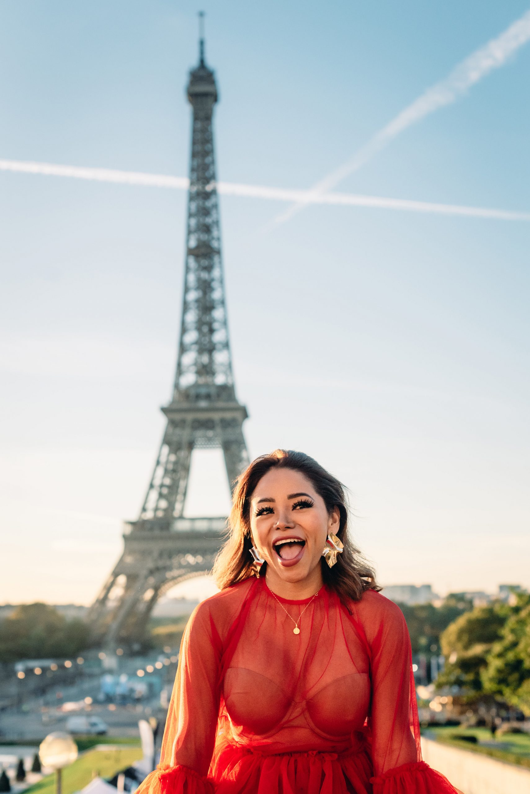 Portrait photography session in front of the Eiffel Tower in Paris, featuring a young woman in a mesh red dress and big gold earrings at sunrise