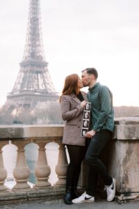 Couple holding their sonogram and kissing for their cute pregnancy announcement photo in front of the Eiffel Tower.